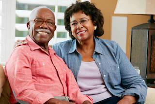 Two smiling adults sitting together in a dental office waiting room or clinical setting.