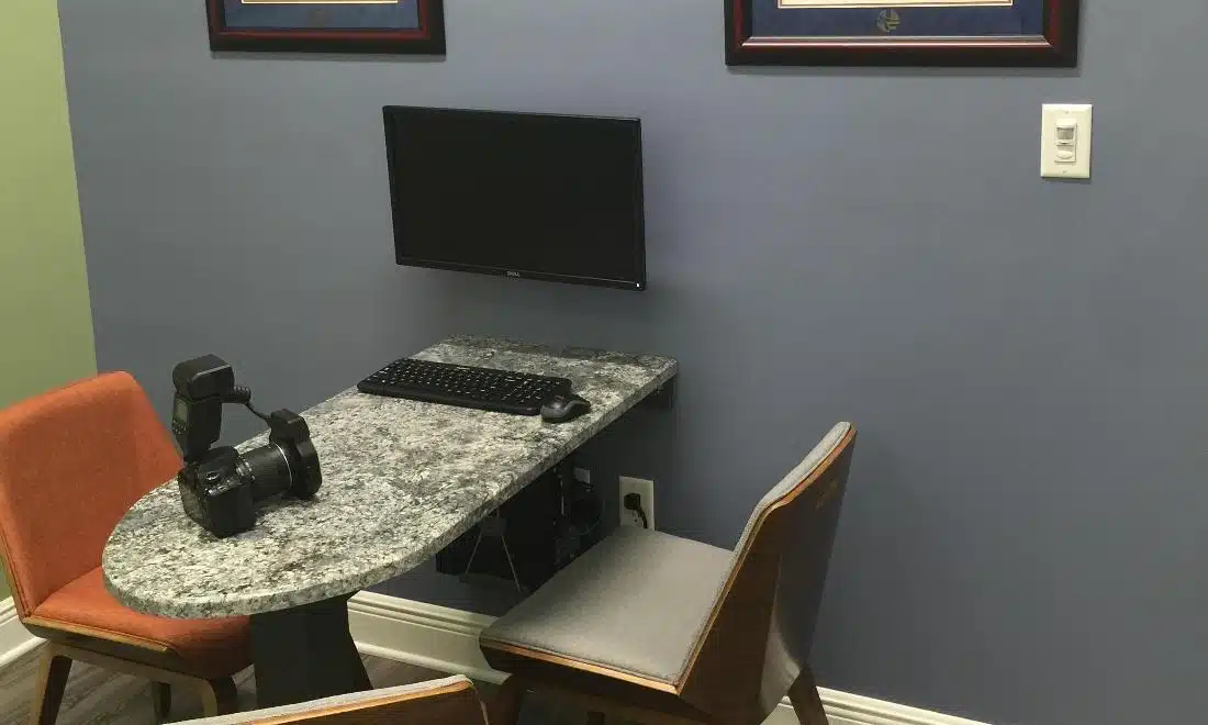 Modern dental office workspace with computer monitor, orange chair, and granite countertop desk.