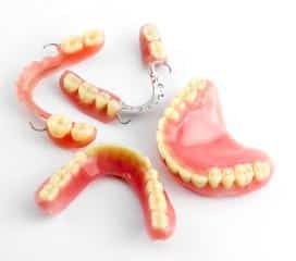 Dental prosthetics and dentures displayed on white surface, showing various artificial teeth models and complete denture examples.
