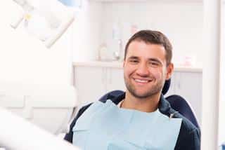 Smiling male patient in dental chair wearing bib at Groves Dental Care office