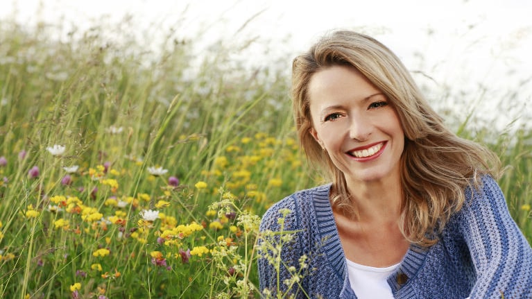 Woman smiling outdoors in wildflower field wearing blue cardigan for dental care website.