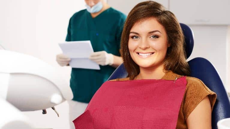Smiling woman in dental chair with dentist and assistant in background at dental office.