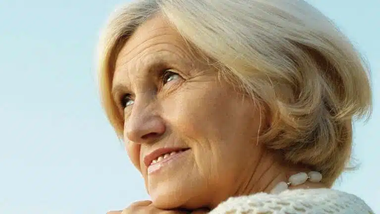Smiling older woman with gray hair against blue sky background for dental care website.