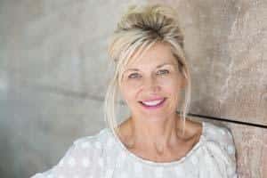 Professional woman smiling at camera in clinical dental office setting wearing white top.