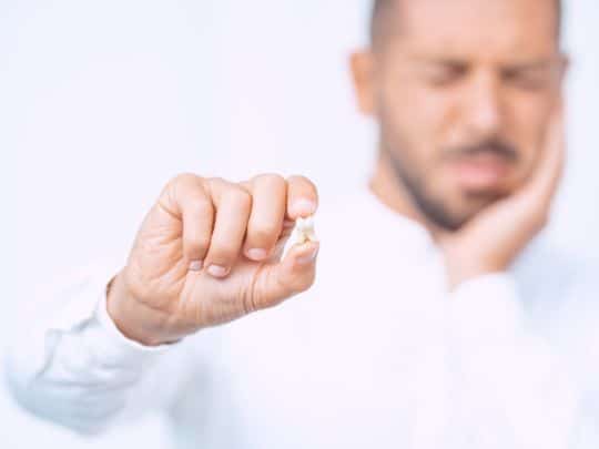 Man in white shirt making fist gesture against blurred background in dental care context.