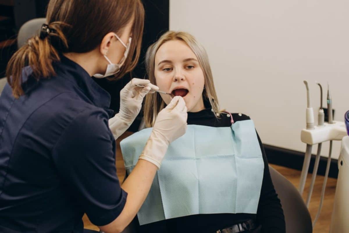 Dental hygienist examining patient's teeth in clinical treatment room setting.
