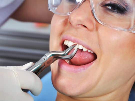 Patient receiving dental treatment with suction tool in dental office chair