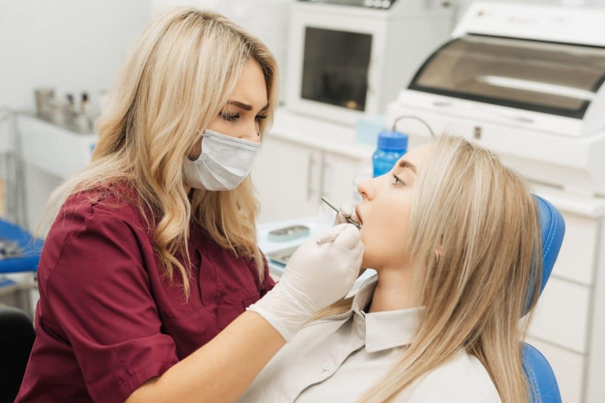 Dentist in maroon scrubs examines young patient's teeth in modern dental office operatory.