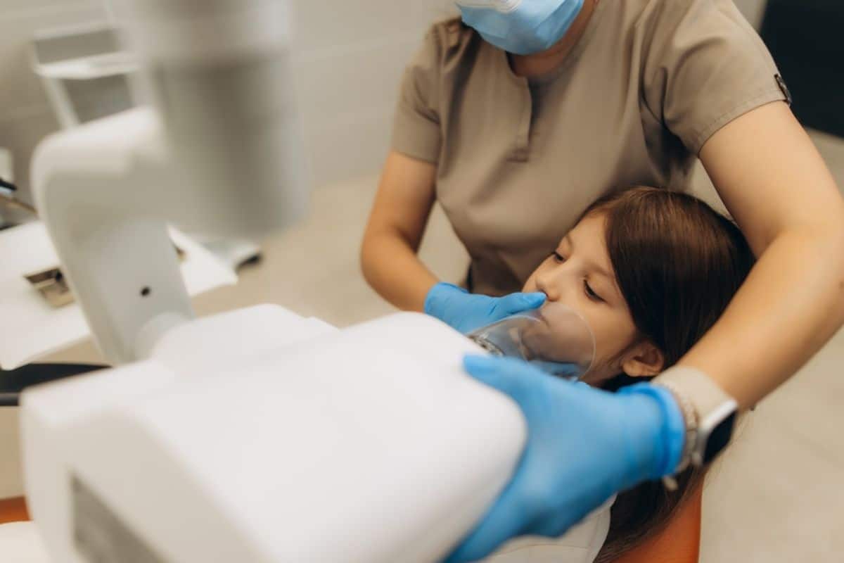 Dentist in blue gloves examining patient's teeth in dental clinic treatment chair.