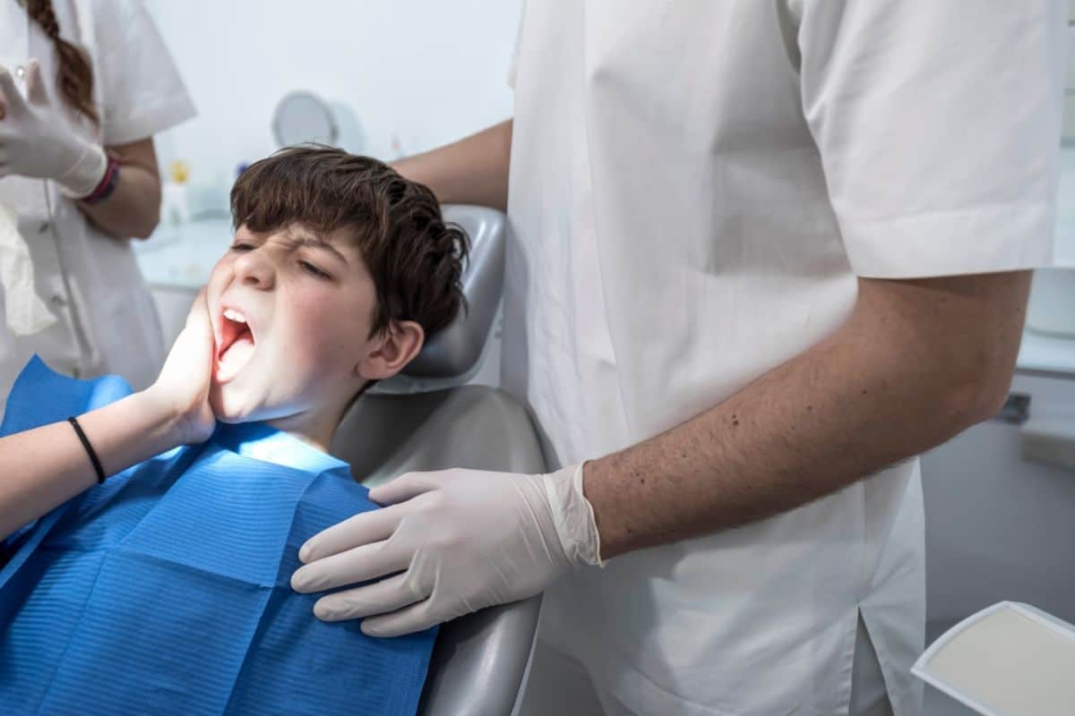 Pediatric dentist examining young child's mouth during dental checkup in clinical setting.