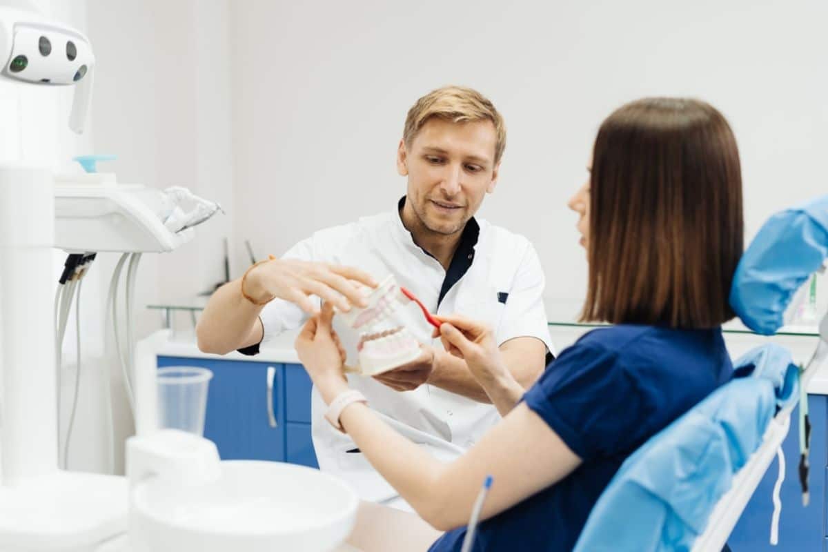 Male dentist showing female patient dental model in bright clinical treatment room.