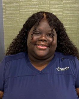 Woman in blue Groves Dental Care scrubs smiling at camera, professional headshot indoors.